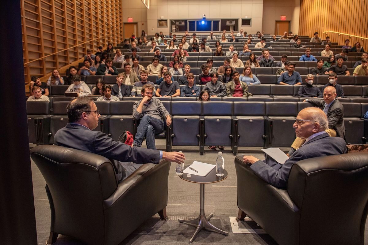 A view from behind Professor Jeremy Siegel and Matt Levine, facing an audience in an auditorium.