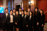 A group of people, mostly dressed in black formal wear, pose for a group photo