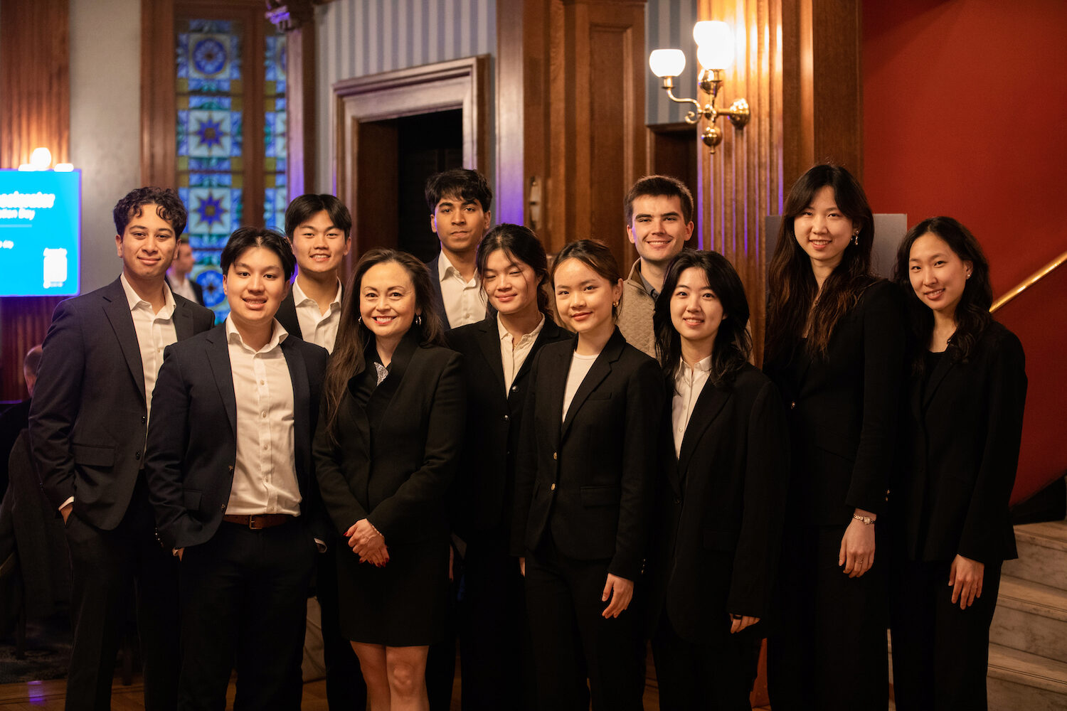 A group of people, mostly dressed in black formal wear, pose for a group photo