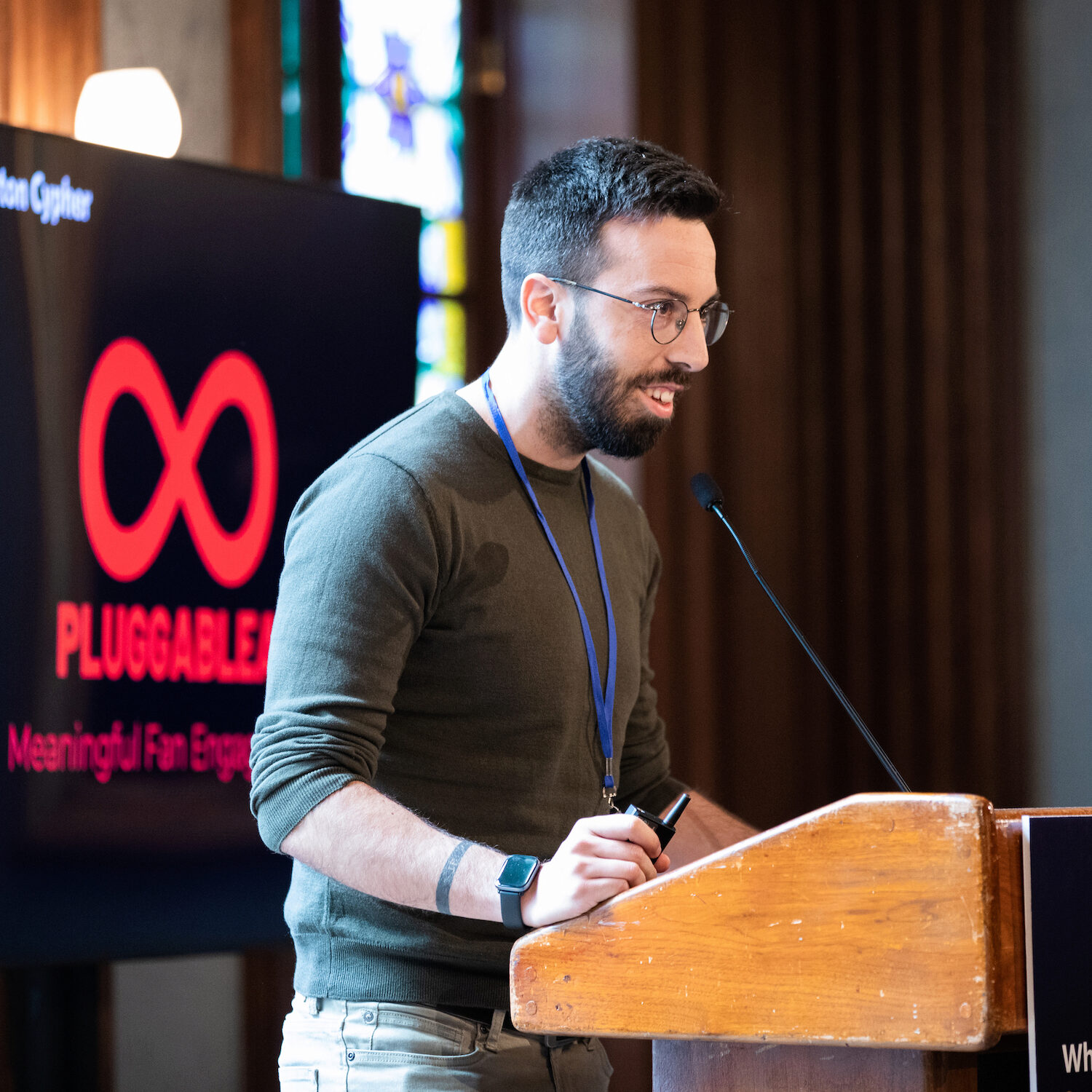 A speaker at a podium in front of a black screen that says PluggableAI