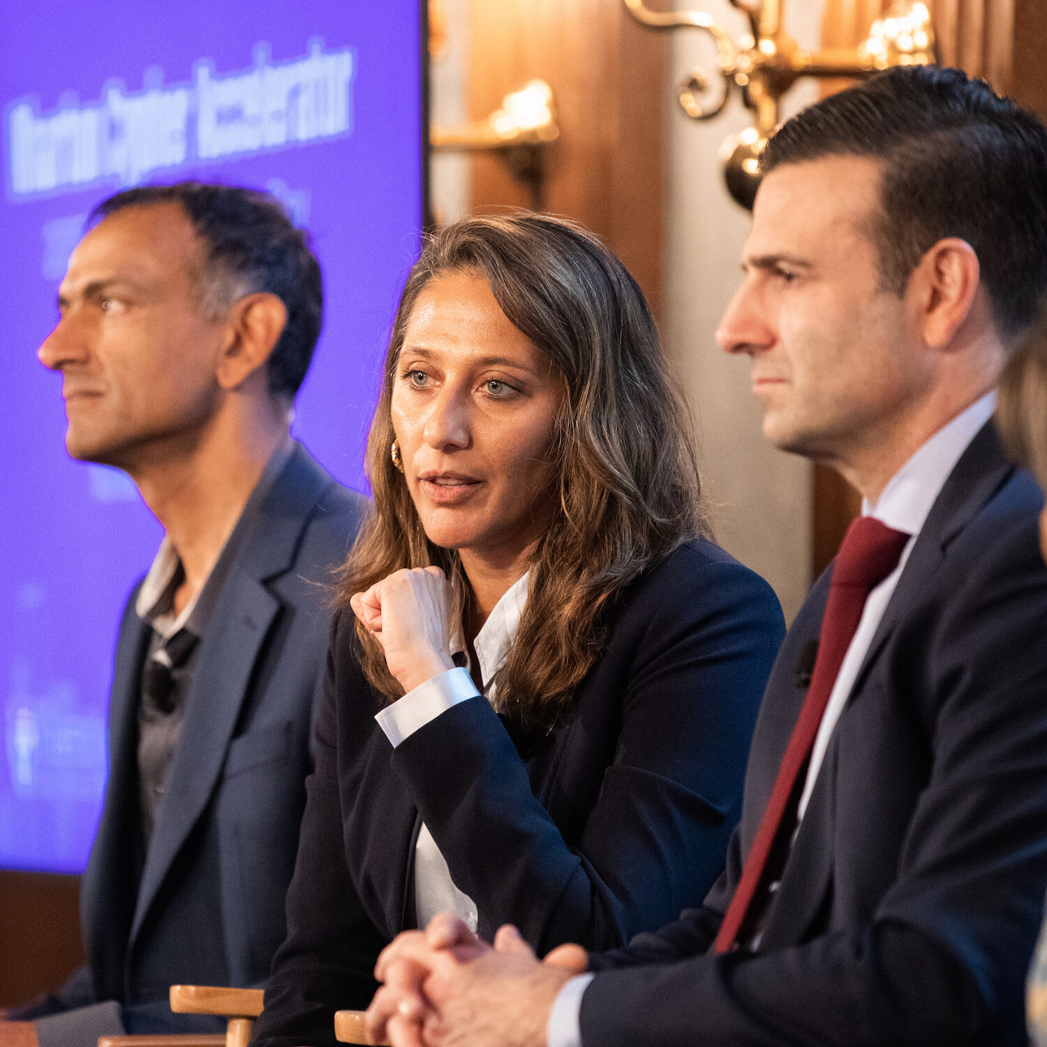 A panelist speaks while seated, as two other panelists react
