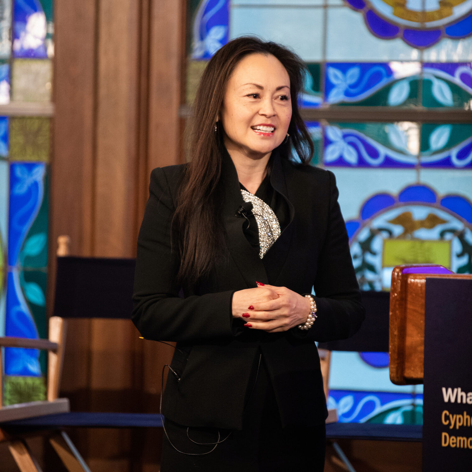 A person speaking in front of a podium and a stained glass window background.
