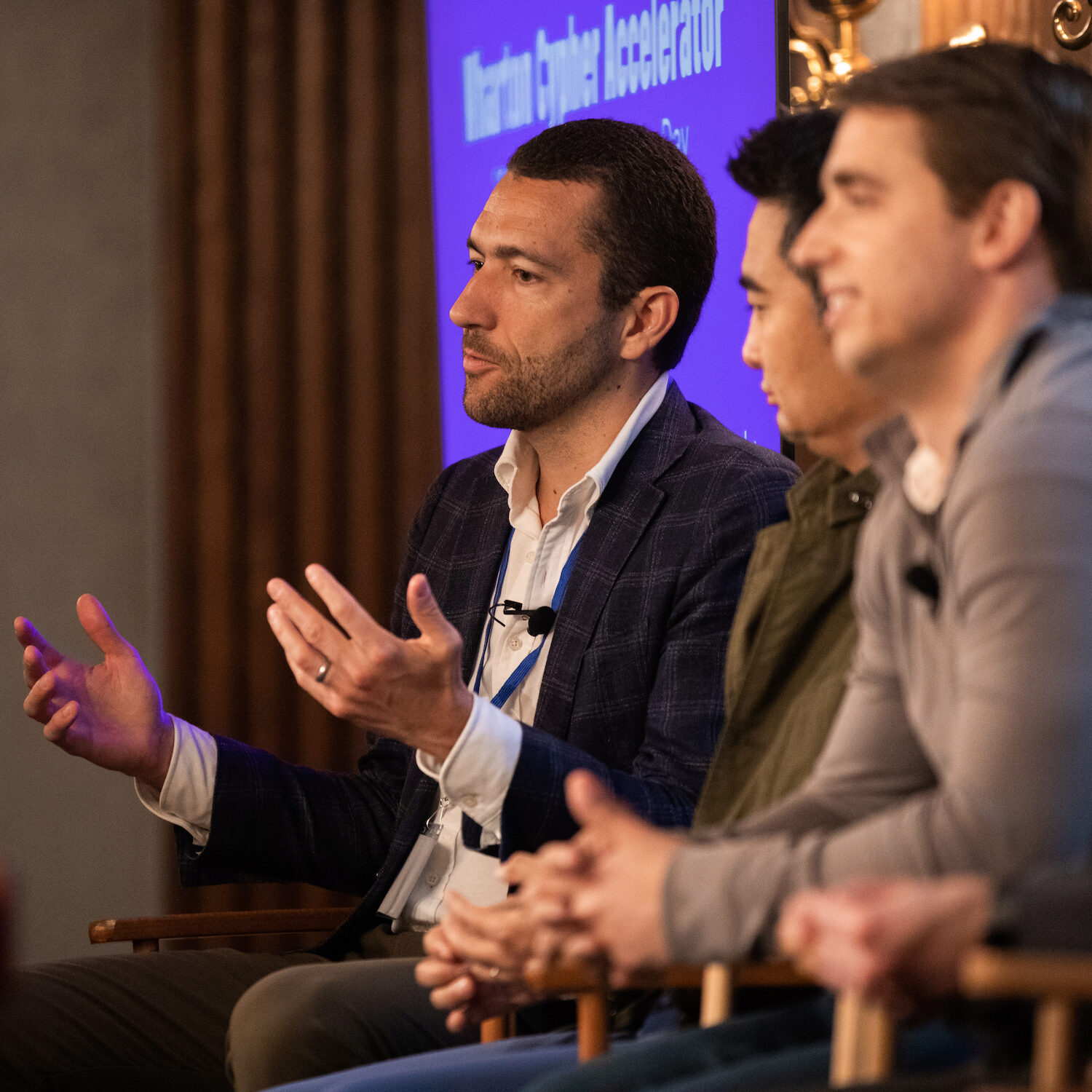 A Demo Day speaker gestures with his hands while speaking from a seated position, as other panelists react.